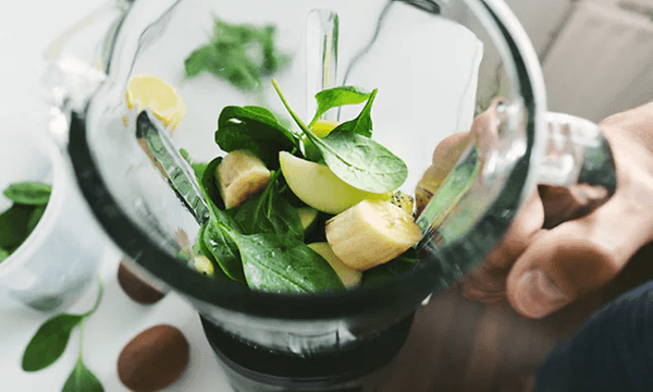 en blender fylt med oppkuttet frukt og blader