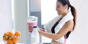 Kvinna iträningskläder tillagar en rosa smoothie i en blender.