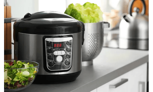 En sort slow cooker på et køkkenbord med grøn salat foran