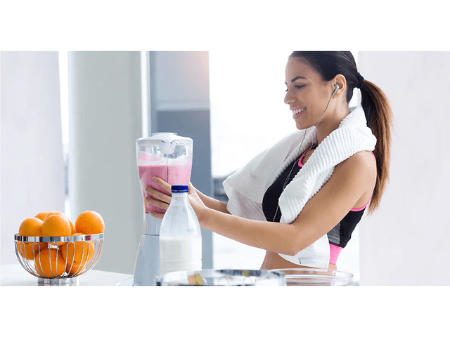kvinde i sportstøj laver pink smoothie med en blender