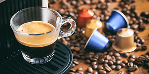 En kopp espresso fra en kapselmaskin med kapsler og kaffebønner på kjøkkenbenk