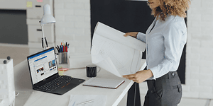 Kvinnelig arkitekt ser på en tegning med Lenovo ThinkPad ved siden av henne på et bord