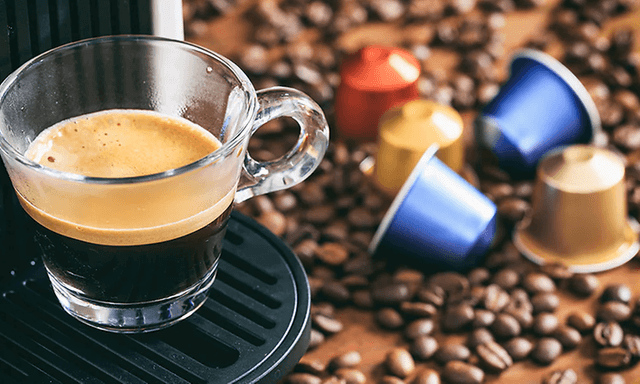 Espressokupillinen kapselikoneesta, jonka vieressä on  kahvikapseleita ja kahvipapuja