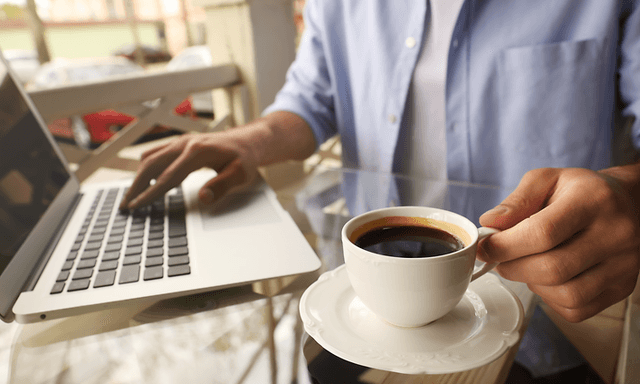 En person som jobbar på en bärbar dator med en kopp kaffe bredvid. 