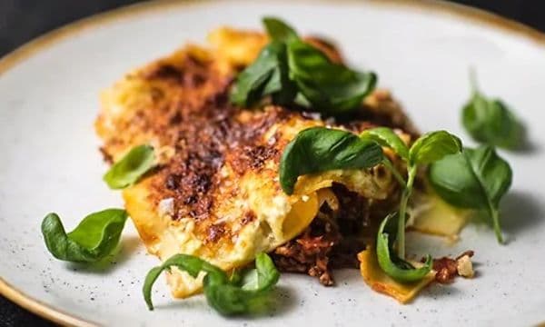 Lasagne på en vit tallrik med basilika blad på. 