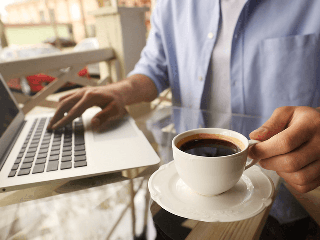 person sitter med en full kaffekopp og jobber på en bærbar pc