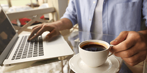 person sitter med en full kaffekopp og jobber på en bærbar pc