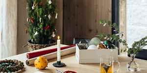 julepynt og innpakning til julegaver på et bord med levende lys og et juletre i bakgrunnen