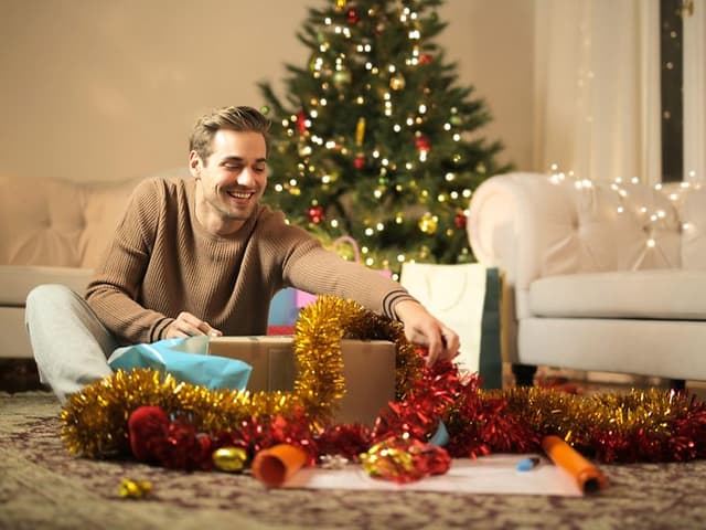En man öppnar en julklapp som han fått av sin partner - Julklappar till pojkvän