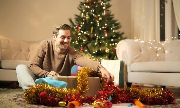 En man öppnar en julklapp som han fått av sin partner - Julklappar till pojkvän
