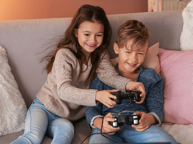To barn som spiller TV-spill sammen i en sofa