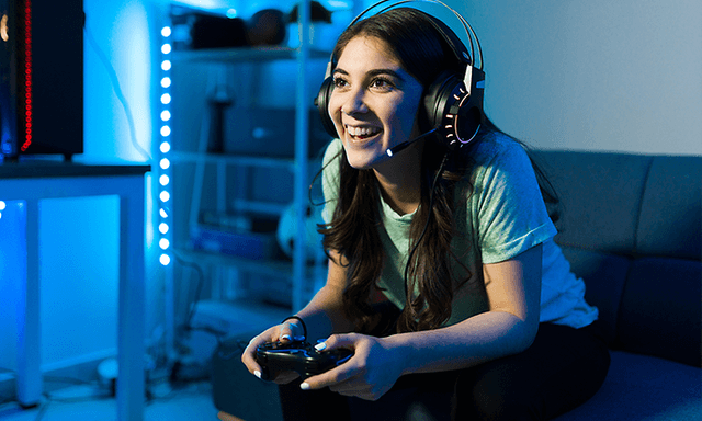 Kvinne med headset som sitter i sofaen og gamer