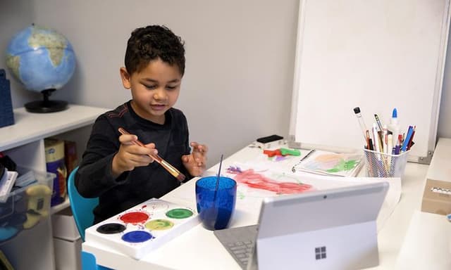 Lille dreng maler ved et bord med en Surface laptop