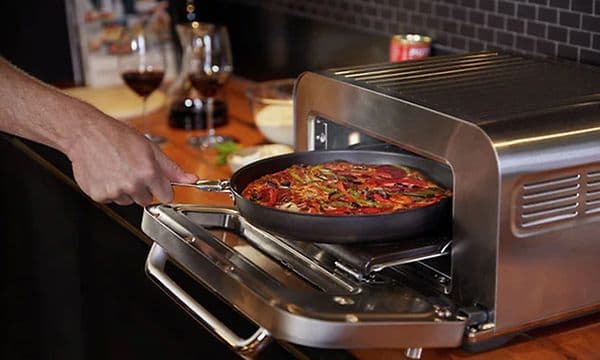 Person som trekker panne ut av Sage PIzzaiolo pizzaovn
