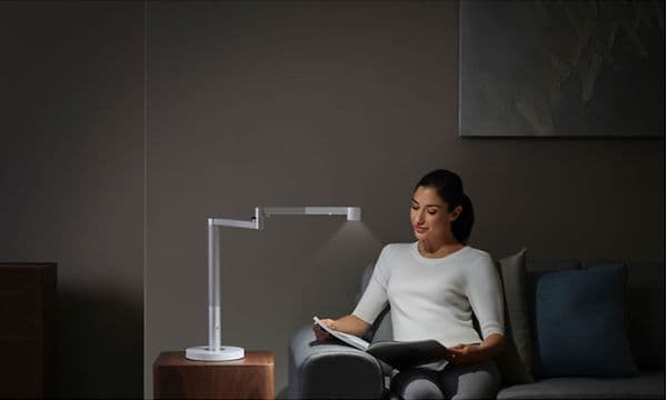 Kvinde sidder i en sofa og læser i et blad ved siden af en Dyson-lampe