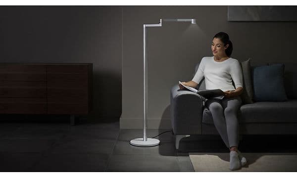 Kvinde sidder i en sofa og læser i et blad ved siden af en Dyson-lampe