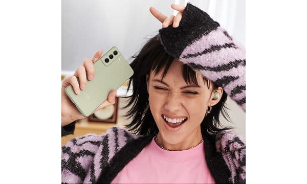 Samsung Galaxy S21 FE i hånden på kvinde, som lytter til musik og laver dansebevægelser