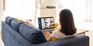 Woman sitting on couch while attending a meeting on her laptop
