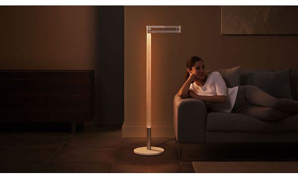 Lightcycle Morph Floor:  Kvinna som ligger på en soffa bredvid en Dyson-lampa.