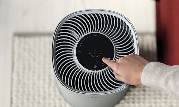Harmaa Electrolux Flow A3 -ilmanpuhdistin kuvattuna ylhäältä sekä käsi painamassa ohjauspaneelin nappia