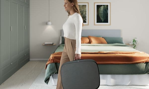 A lady in a living room carrying a big dark grey Well 5 like a suitcase