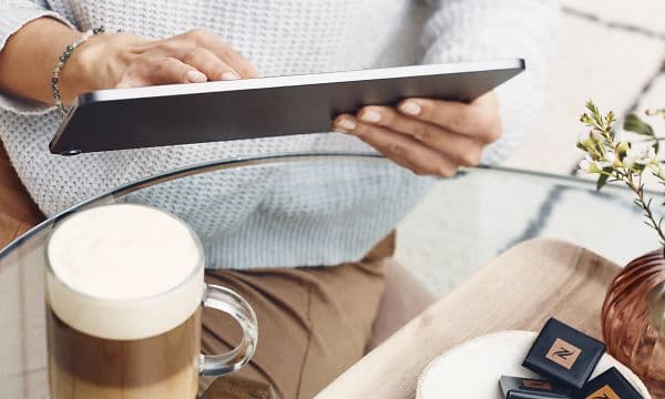 en person sitter med et nettbrett ved et bord med kaffe og kjeks