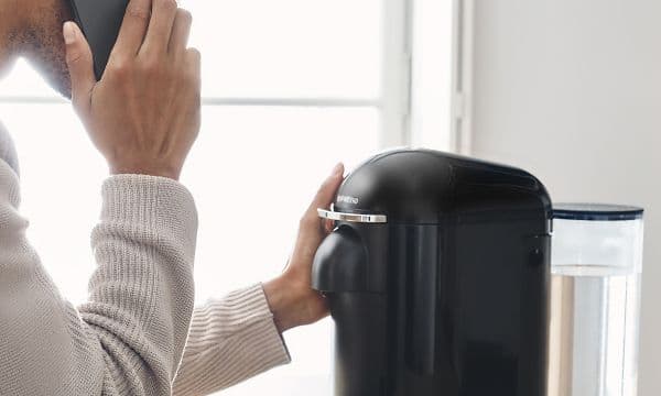 en mann holder en telefon mens han holder på sin nespresso kapselmaskin