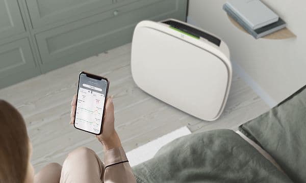 Valkoinen Well 5 -ilmanpuhdistin lattialla ja Wellbeing-sovellus henkilön puhelimessa