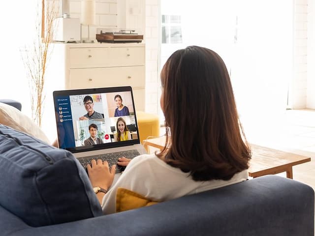 Kvinna sitter på en soffa och deltar i ett digitalt möte på sin dator