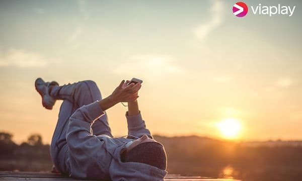 Streamingtjänster hos Elgiganten: Viaplay banner. Kvinna ligger på ryggen med mobilen i händerna