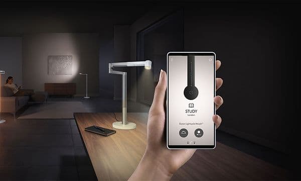 en kvinne sitter på en sofa mens en hånd I forgrunnen holder en smarttelefon med Dyson-appen åpen