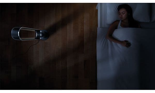 En kvinne ligger i sengen og sover ved siden av en Dyson Cool tårnvifte.