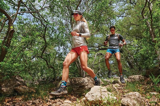 Garmin Fenix 7 på armene på en kvinde og en mand, der løber i vildmarken