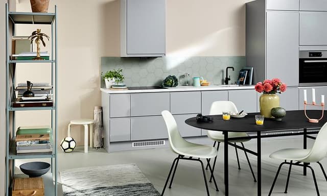 Ljusgrått EPOQ Integra kök med öppen planlösning, ett svart köksbord med vita stolar och en bokhylla.