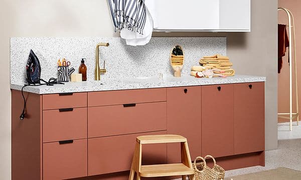 Tvättstuga från EPOQ Trend i korallfärg med vita skåp och öppen planlösning med guldfärgad kran och tvättho.