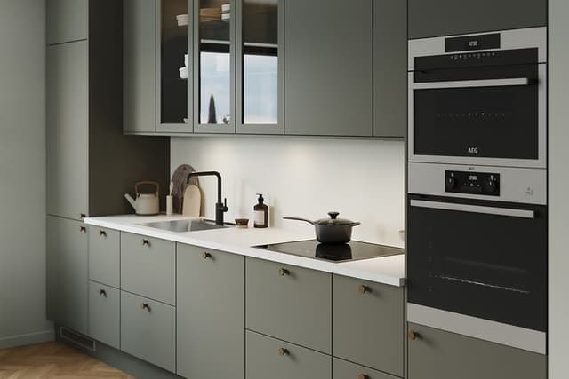 Mossgrönt kök från EPOQ Trend med vit bänkskiva, integrerade vitvaror, svart kran och vitrinskåp.