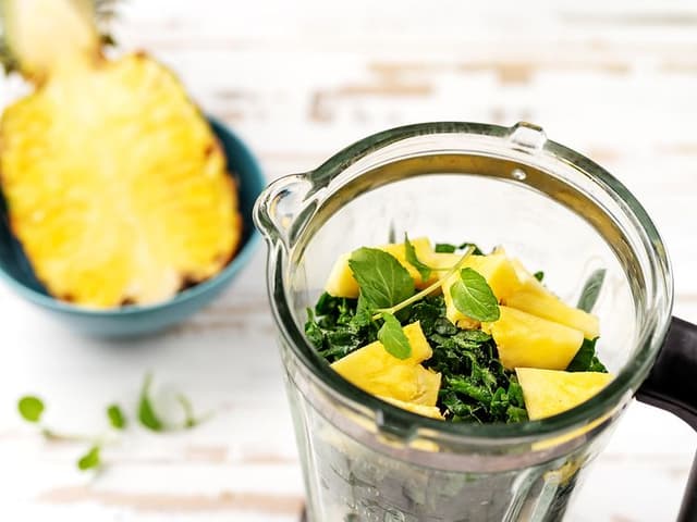 Halv ananas bredvid en blender med spenat och ananas