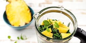 En halv ananas ved siden av en blender med grønt og ananas