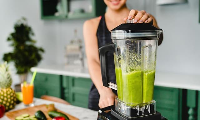 Kvinne som lager en grønn smoothie med en blender