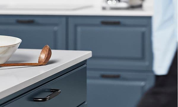 Epoq Heritage Blue Grey kjøkken med kjøkkenøy og hvit benkeplate, tresleiv og en hvit skål på toppen