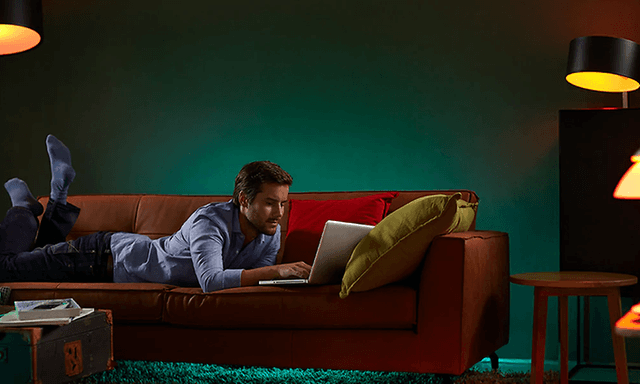 Man ligger på soffa och använder bärbar dator med olika smartlampor runt sig