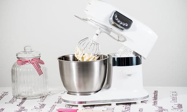 En hvit kjøkkenmaskin, en glasskrukke og en slikkepott på et bord