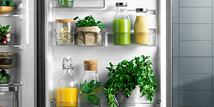 Avoin Electrolux-jääkaappi ja sen sisällä apelsiinimehua, vihersmoothieta ja tuoreita yrttejä 