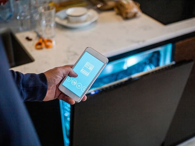 Hånd med smartphone foran halvåben opvaskemaskine