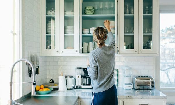 Kvinde sætter ting på plads i sine køkkenskabe