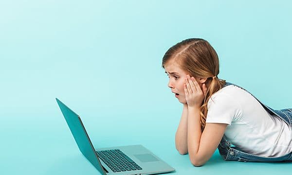Jente ligger på magen foran en PC