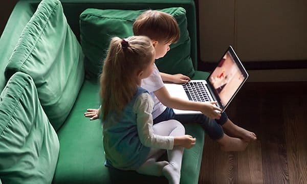 En gutt og en jente som sitter på en sofa med en PC