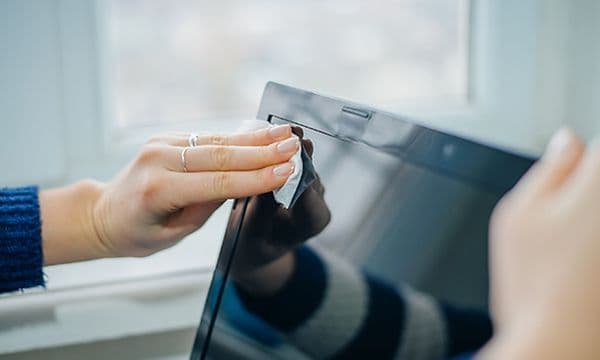 En person vasker skjermen på en laptop med en klut
