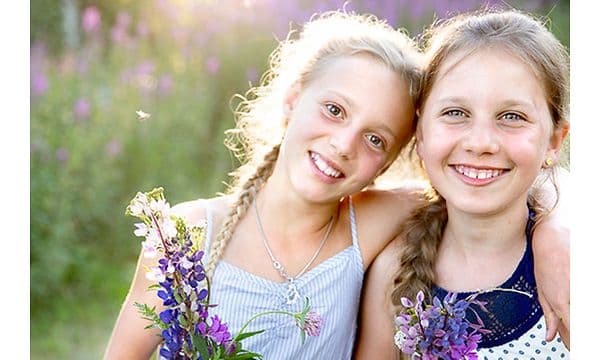 To jenter i en blomstereng som smiler med sterkt sollys bak
