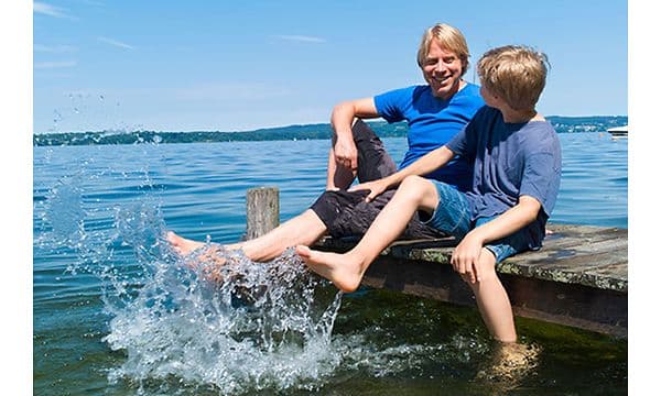 En mann og et barn sitter på en brygge og plasker med føttene i vannet